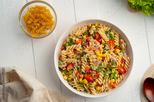 Homemade macaroni salad with trivelle pasta and canned tuna, carrot, Head Lettuce, tomato, corn and mayonnaise dressing in a white plate on wooden table.Top view