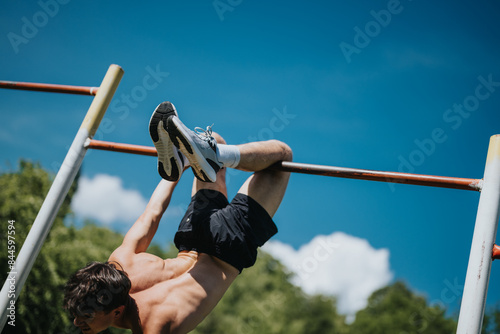 Fotografie A young man working out in nature, performing calisthenics on a pull-up bar, showcasing physical strength and wellness under a clear blue sky