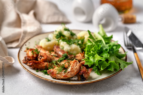 Obraz na płótnie Baked or fried chicken necks in barbecue sauce, cauliflower and lettuce leaves on a plate on the table. A healthy dinner on a light gray background in closeup. Proper nutrition w salonie