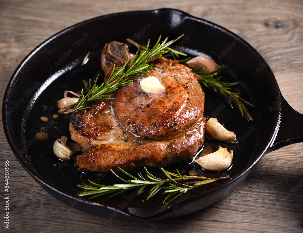 Pork cutlet on the bone in a piece of butter with garlic and rosemary in a frying pan Pork cutlet on the bone in a piece of butter with garlic and rosemary in a frying pan