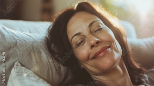 A woman with closed eyes a gentle smile and long hair resting her head on a soft pillow basking in warm sunlight.