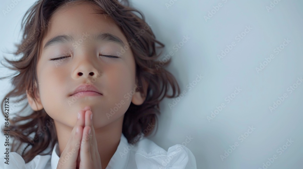 Young child with eyes closed hands clasped in prayer against a soft-focus white background evoking a sense of innocence and spirituality. Young child with eyes closed hands clasped in prayer against a soft-focus white background evoking a sense of innocence and spirituality.