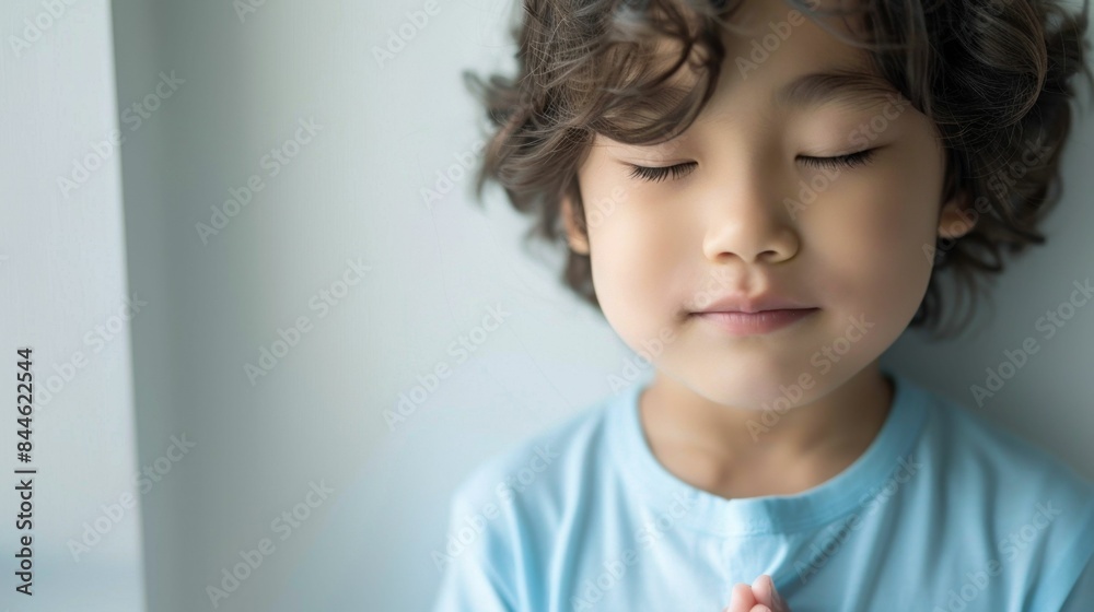 Young child with eyes closed possibly in a state of relaxation or prayer wearing a light blue shirt with soft curly hair against a neutral background. Young child with eyes closed possibly in a state of relaxation or prayer wearing a light blue shirt with soft curly hair against a neutral background.