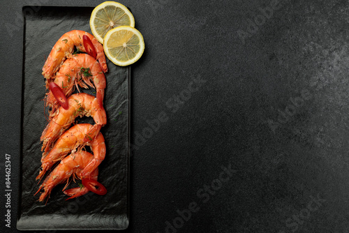 Large cooked king prawns on a black background. Lemon slices