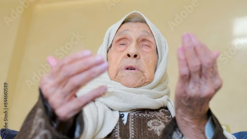Close up shot for old lady raising her hand praying allah in warm theme closing her eyes crying and looking for his mercy photo