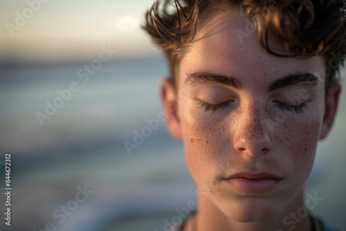 Close up of a young man, eyes closed, deeply meditating on a serene ocean shore.