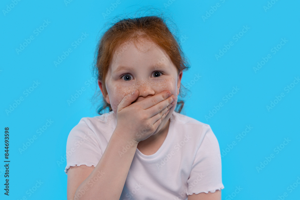 Young Girl Covering Mouth With Hand Against Blue Background Young Girl Covering Mouth With Hand Against Blue Background