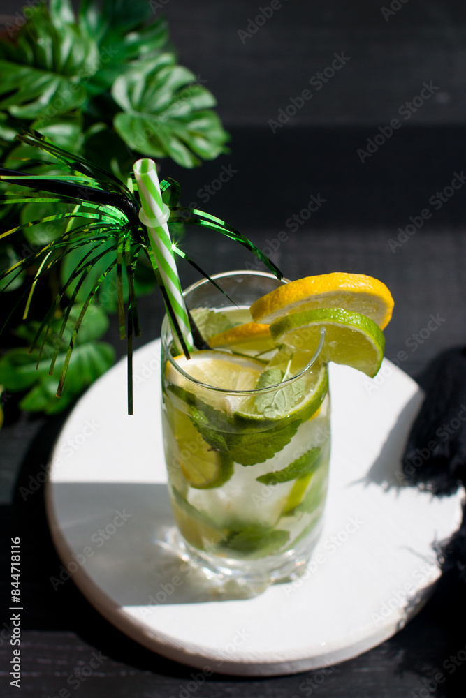 Fototapeta premium citrus lemon drink with lime in a glass with a straw, mint and ice. Refreshing drink, freshly squeezed refreshing juice
