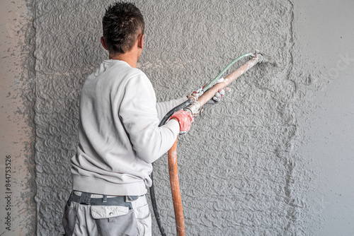 Machine plastering. Applying gypsum plaster by mechanized method on a wall. A worker hand removes excess plaster with leveler.
