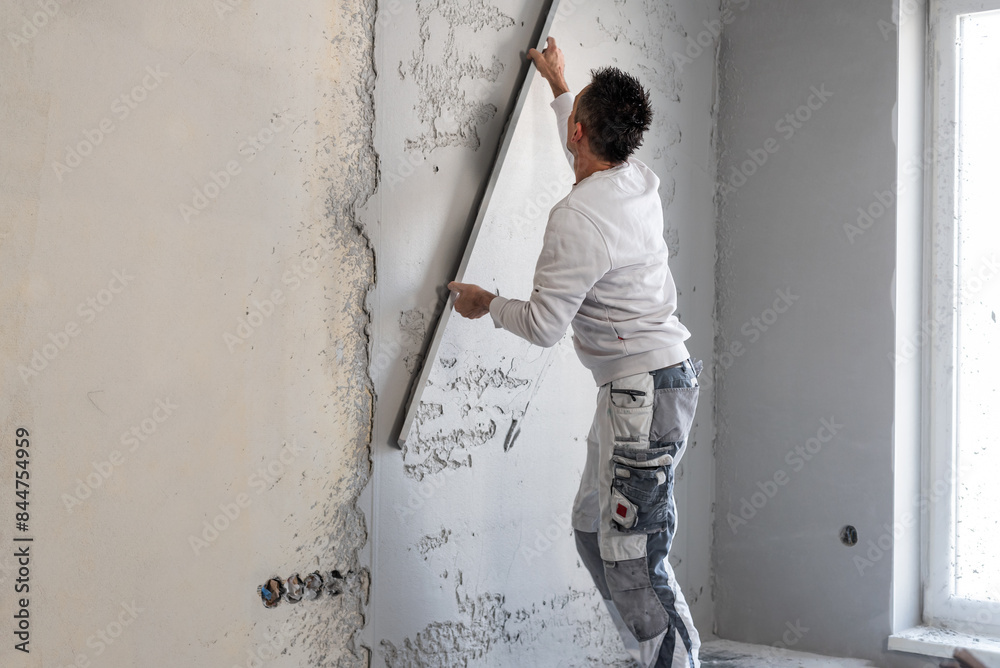 Machine plastering. Applying gypsum plaster by mechanized method on a wall. A worker removes excess plaster with leveler. Machine plastering. Applying gypsum plaster by mechanized method on a wall. A worker removes excess plaster with leveler.