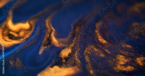 Ink spill. Glitter fluid mix. Defocused blue gold color glowing sparkling marble texture acrylic wave dark abstract art background.