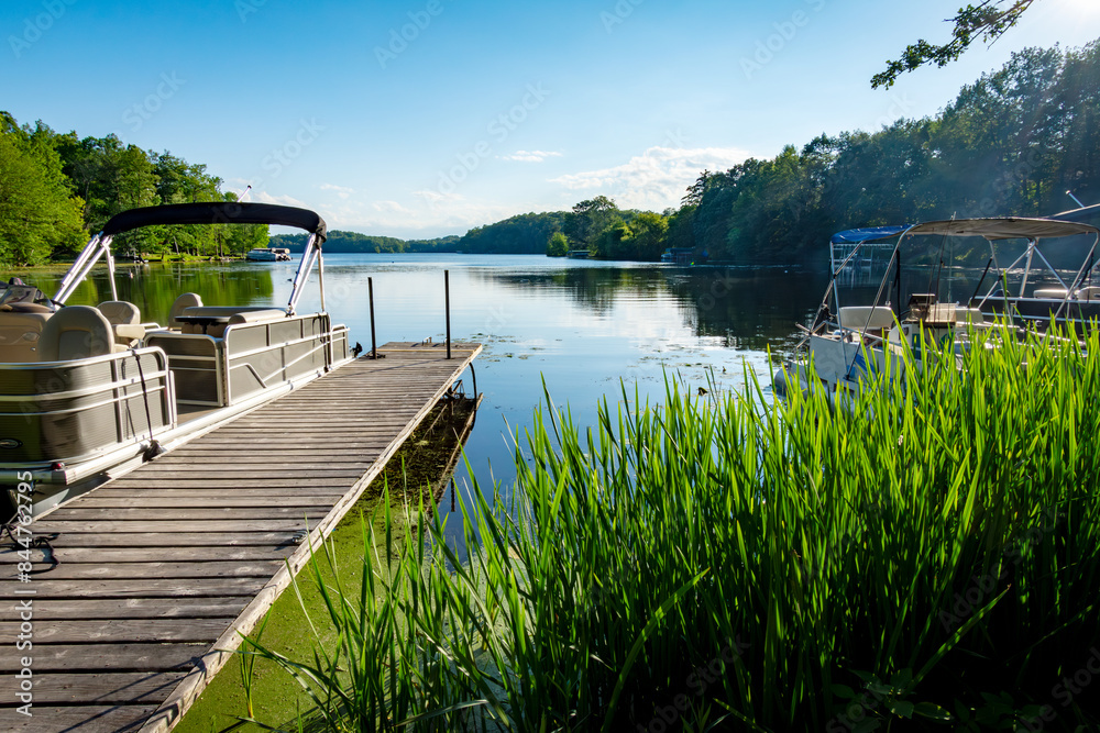 Looking out onto a Wisconsin lake in the late afternoon on a calm day from the shore with a  pontoon boat  by the side of a pier.