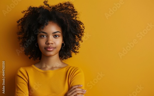 A woman with curly hair is standing in front of a yellow wall. She is wearing a yellow shirt and has her arms crossed © imagineRbc
