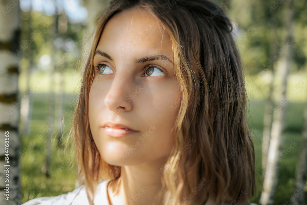 Close-up of a womans face with green eyes, showing a natural and serene expression. The background features blurred greenery, enhancing the focus on her facial features. Close-up of a womans face with green eyes, showing a natural and serene expression. The background features blurred greenery, enhancing the focus on her facial features.