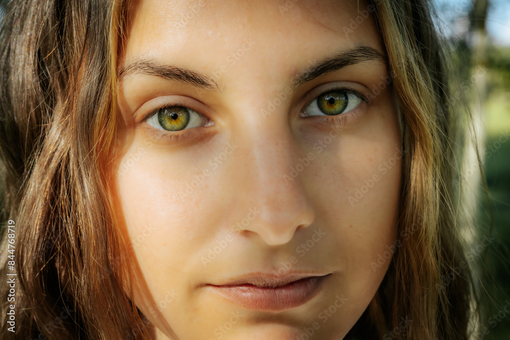 Fototapeta premium Intimate close-up of a womans face highlighting her striking green eyes and natural complexion, with a serene expression and natural background.