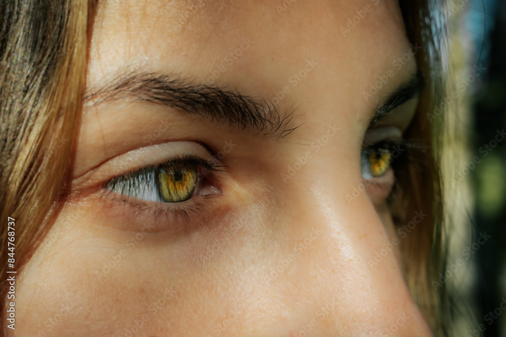 Fototapeta premium Intimate close-up of a womans face highlighting her striking green eyes and natural complexion, with a serene expression and natural background.