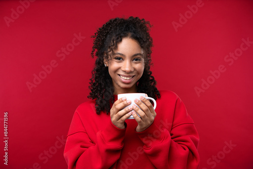 Portrait of a young girl smiling at the camera while standing against a red background. 