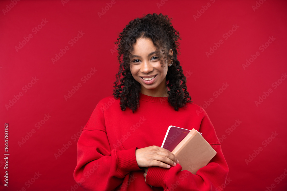 Portrait of a young girl with notebook smiling at the camera while standing against a red background. Portrait of a young girl with notebook smiling at the camera while standing against a red background.