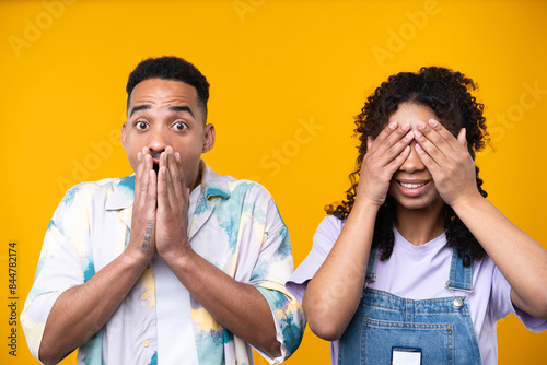 Two hipster friends smiling cheerfully while standing against a yellow background.