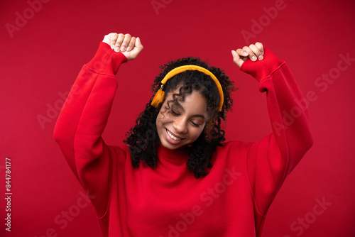 Portrait of a young girl with headphone smiling at the camera while standing against a red background. 
