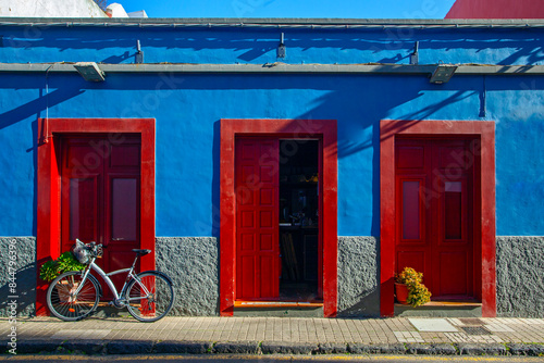 Buildings, street and parked bicycle on blue sky background. Colonial style of the city. Houses painted with various bright colors. Red barrels
