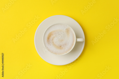 Tasty cappuccino in coffee cup on yellow background, top view