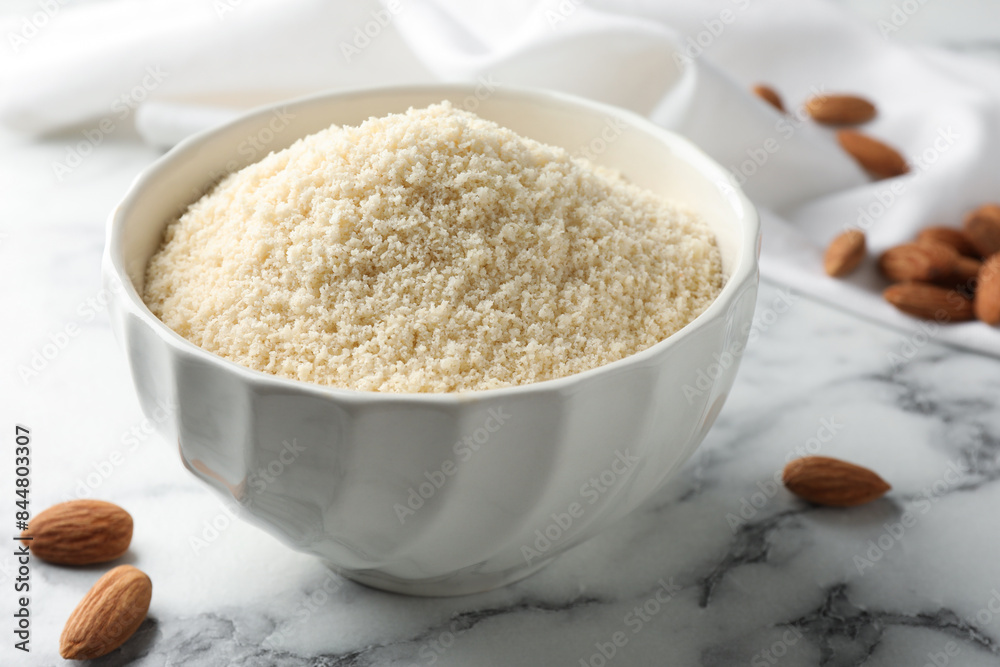 Fresh almond flour in bowl and nuts on white marble table, closeup Fresh almond flour in bowl and nuts on white marble table, closeup