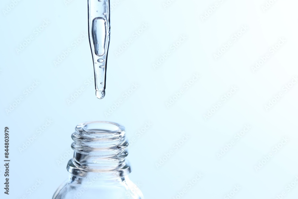 Dripping liquid from pipette into glass bottle on light blue background, closeup. Space for text Dripping liquid from pipette into glass bottle on light blue background, closeup. Space for text