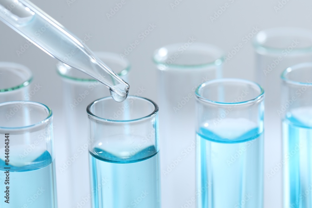 Dripping liquid from pipette into test tube on light background, closeup Dripping liquid from pipette into test tube on light background, closeup
