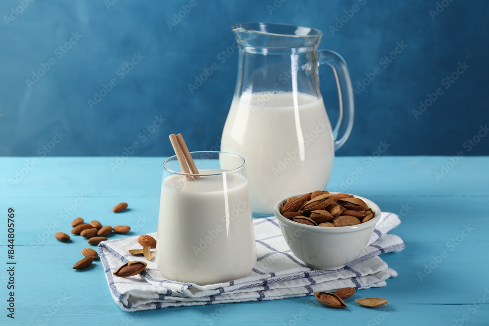 Glass of almond milk, jug and almonds on light blue wooden table Glass of almond milk, jug and almonds on light blue wooden table