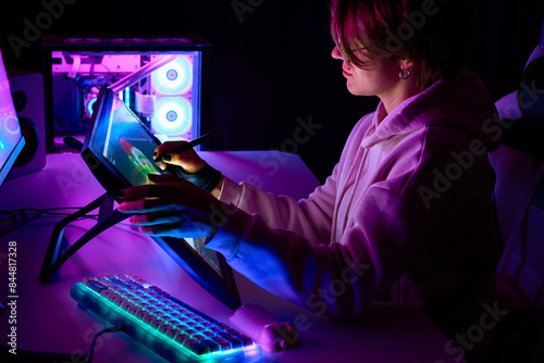 Female designer works on a Drawing tablet with Screen. A woman in a room with neon lighting draws with a stylus on a graphics tablet. 3D artist is working on a project