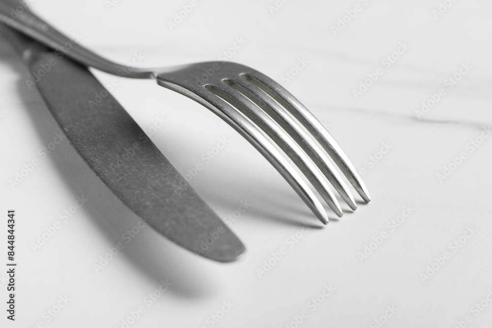 Stylish cutlery. Silver knife and fork on white marble table, closeup Stylish cutlery. Silver knife and fork on white marble table, closeup