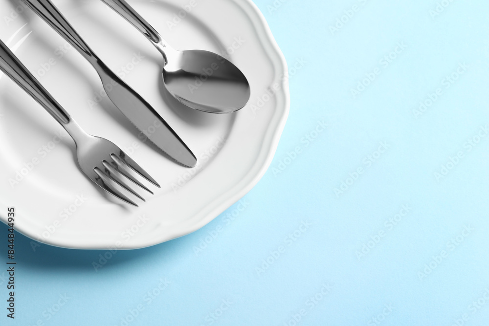 Stylish silver cutlery and plate on light blue background, above view. Space for text Stylish silver cutlery and plate on light blue background, above view. Space for text