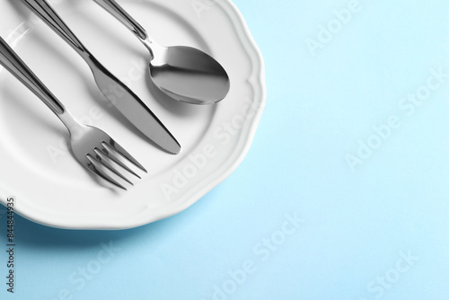 Stylish silver cutlery and plate on light blue background, above view. Space for text