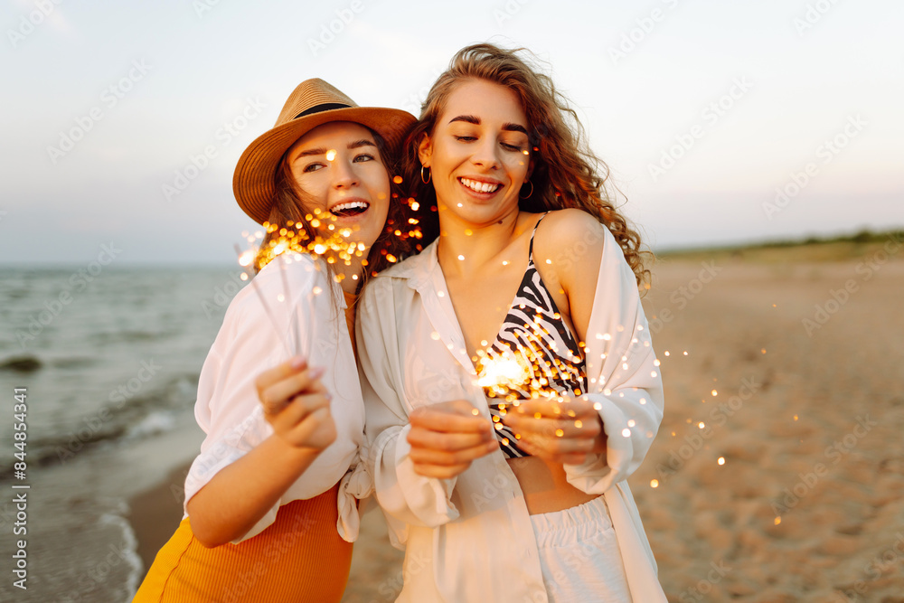 The sparklers in the hands of young woman on the beach. Two women holding sparkles celebrating on beach. Summer holidays, party, vacation, relax and lifestyle concept.
