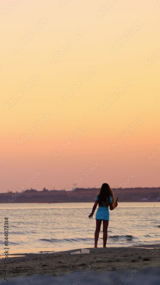 Girl walking in sea water waves on the beach at beautiful sunset. Back view of a little girl with long hair at the seaside in the evening. Vertical video Girl walking in sea water waves on the beach at beautiful sunset. Back view of a little girl with long hair at the seaside in the evening. Vertical video