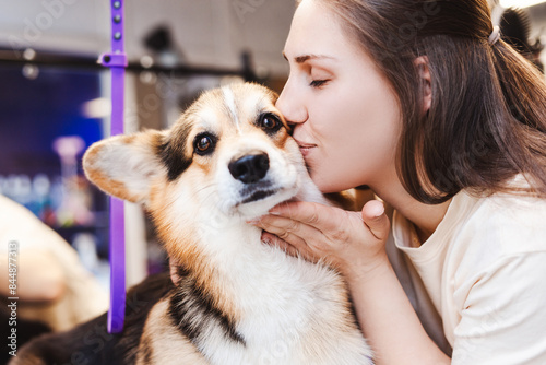 Happy groomer kissing small corgi dog after procedure at her grooming salon