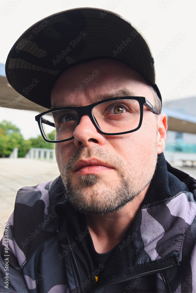Portrait of handsome serious looking young man with glasses, beard and cap, people background
