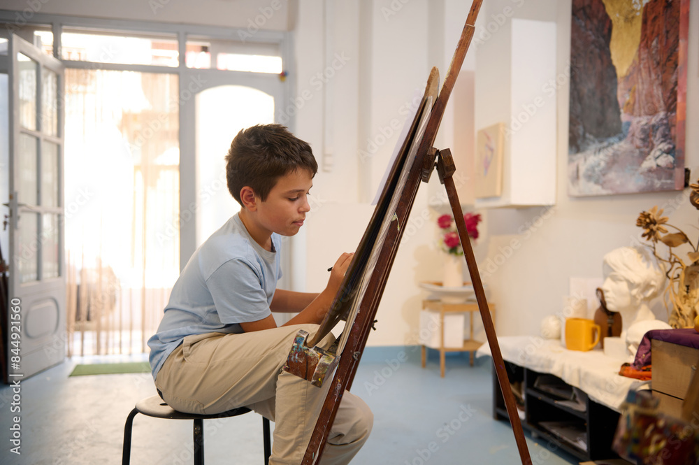 Obraz premium Young boy participating in art class drawing on an easel, learning and creating in a workshop