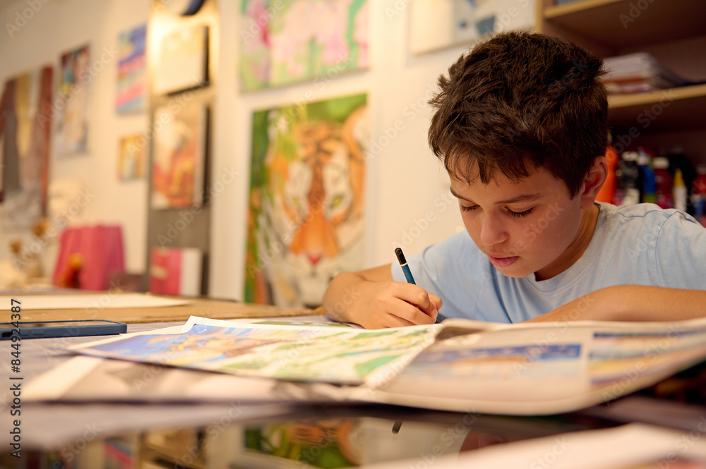 Focused child drawing in art class at a workshop with colorful paintings in the background Focused child drawing in art class at a workshop with colorful paintings in the background