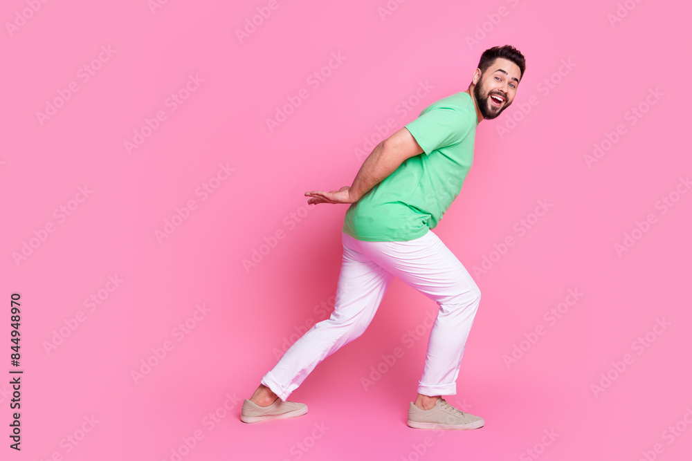 Full size photo of impressed guy dressed green t-shirt white pants hands pull product go empty space isolated on pink color background Full size photo of impressed guy dressed green t-shirt white pants hands pull product go empty space isolated on pink color background