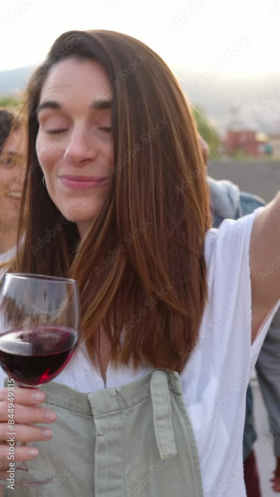 Vertical HD video. Happy beautiful woman smile at camera while dancing and drinking red wine with young group of multiracial friends on the background at summer rooftop party celebration. Vertical HD video. Happy beautiful woman smile at camera while dancing and drinking red wine with young group of multiracial friends on the background at summer rooftop party celebration.
