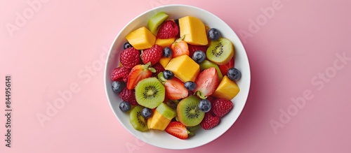 Fresh fruit salad in a bowl on a pink background from above.