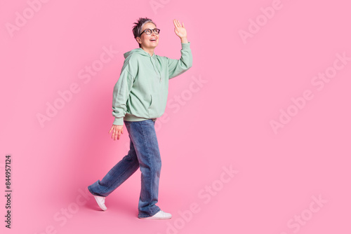 Full length photo of positive funky lady dressed khaki sweatshirt walking waving arm hi empty space isolated pink color background