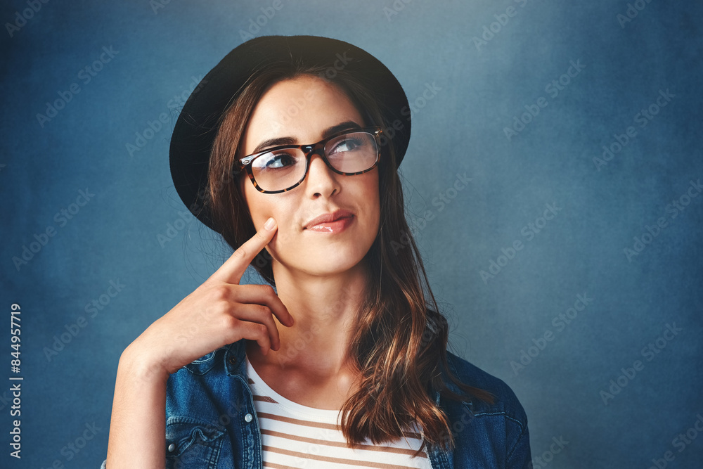 Girl, hat and glasses in studio with thinking of idea for problem solving, solution and planning with mockup. Woman, eyewear and thoughtful with trendy fashion with doubt or unsure on blue background