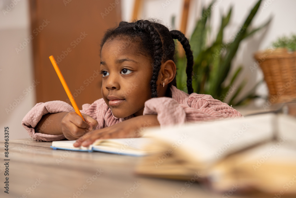 Dreamy African American girl with pen and notepad doing homework Dreamy African American girl with pen and notepad doing homework