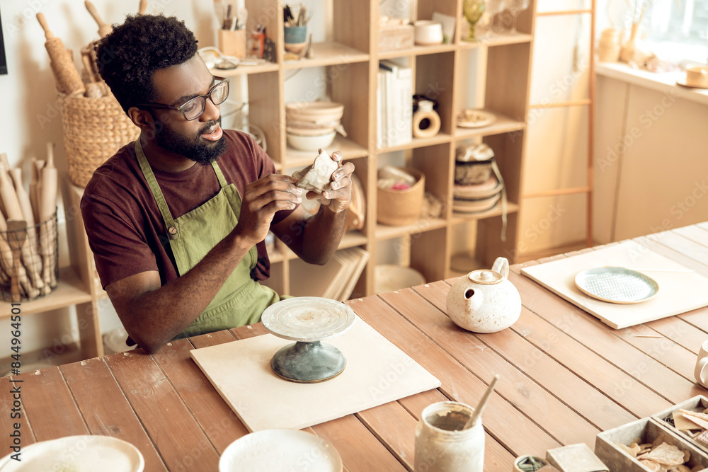 Dark-skinned man at the table with piece of clay in hands Dark-skinned man at the table with piece of clay in hands