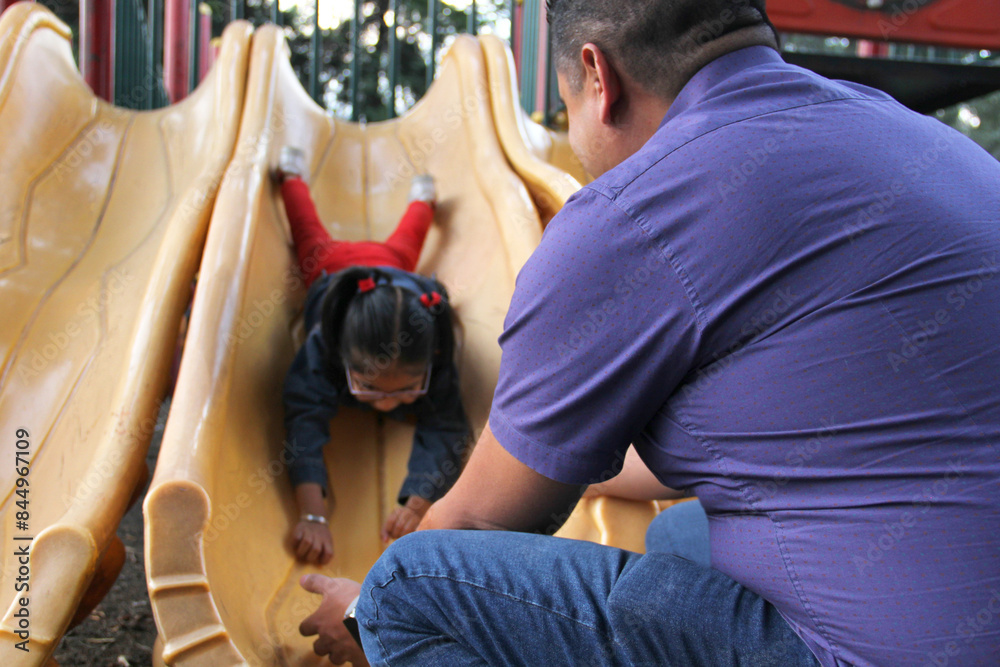 Obraz premium Divorced single dad takes care of his 4-year-old brunette Latina daughter in the park games so she doesn't get hurt and prevent accidents