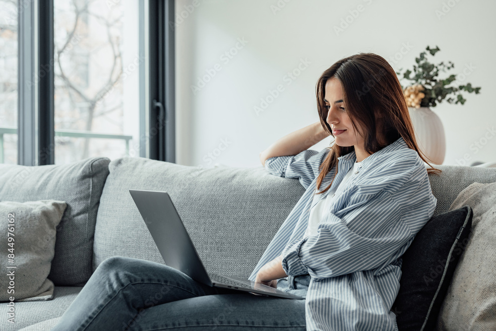 Concentrated millennial girl sit on couch working on laptop browsing internet at home during lazy weekend, focused young woman freelancer busy using computer surfing wireless web shopping online. Concentrated millennial girl sit on couch working on laptop browsing internet at home during lazy weekend, focused young woman freelancer busy using computer surfing wireless web shopping online.