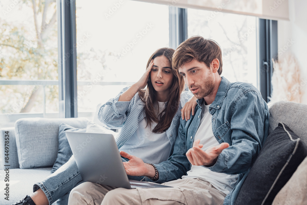 Millennial couple annoyed by stuck laptop or online news sitting together on sofa, frustrated young angry customers confused by computer problem feeling perplexed or puzzled about email message. Millennial couple annoyed by stuck laptop or online news sitting together on sofa, frustrated young angry customers confused by computer problem feeling perplexed or puzzled about email message.